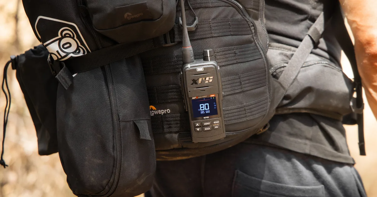 Handheld two-way radio clipped to a hiker's backpack strap