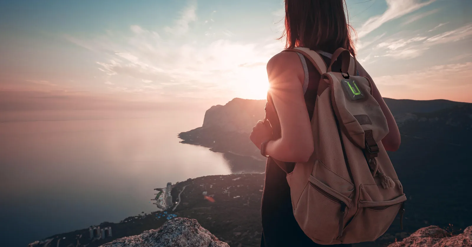 Hiker with a canvas backpack looking out over a coastline at sunset